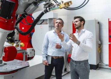 Male engineers discussing over robotic machinery in factory